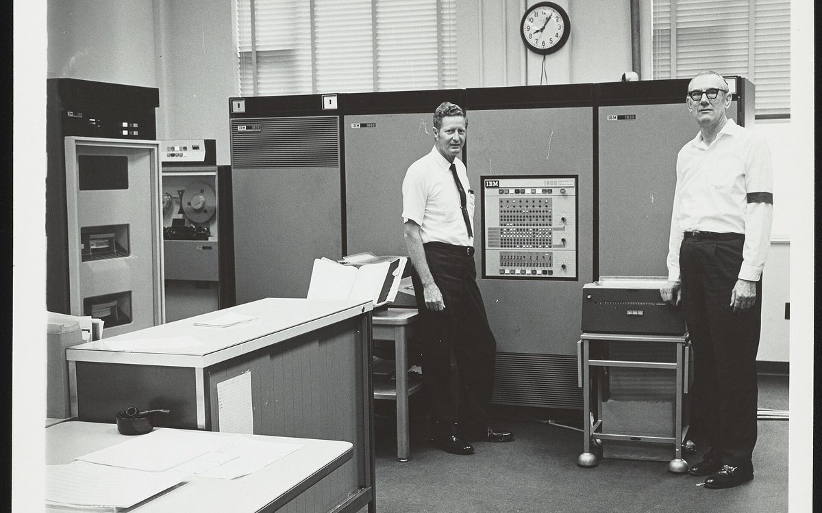 View of the IBM 1800 Data Acquisition and Control System computer used to accept and process data from a mass spectrometer at the Exxon Research and Engineering Company laboratory in Baytown, Texas. This photograph was taken on the day that use of the computer was discontinued at the laboratory. Henry Earle Lumpkin (Research Associate in charge of computer operations) stands to the left while laboratory technician Jack L. Taylor is visible on the right. Taylor is wearing a black band on his right arm to mark the "death" of the computer.